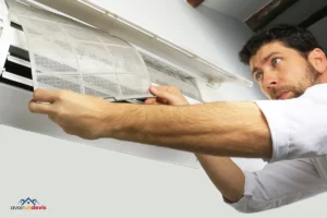 Un homme en chemise blanche travaille méticuleusement sur un climatiseur mural. Il examine ou remplace le filtre, un processus essentiel pour maintenir la qualité de l'air et l'efficacité de l'appareil. Son expression sérieuse et concentrée souligne l'importance de l'entretien régulier de ces systèmes pour garantir leur fonctionnement optimal.